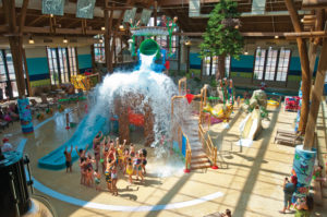 A group of parents and kids smiling as Bish Falls, a giant bucket of water, pours over them at Soaring Eagle Watepark in Mt. Pleasant, Michigan.