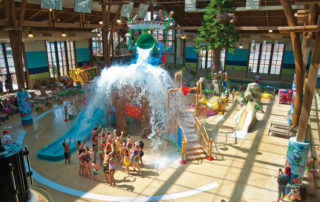 A group of parents and kids smiling as Bish Falls, a giant bucket of water, pours over them at Soaring Eagle Watepark in Mt. Pleasant, Michigan.