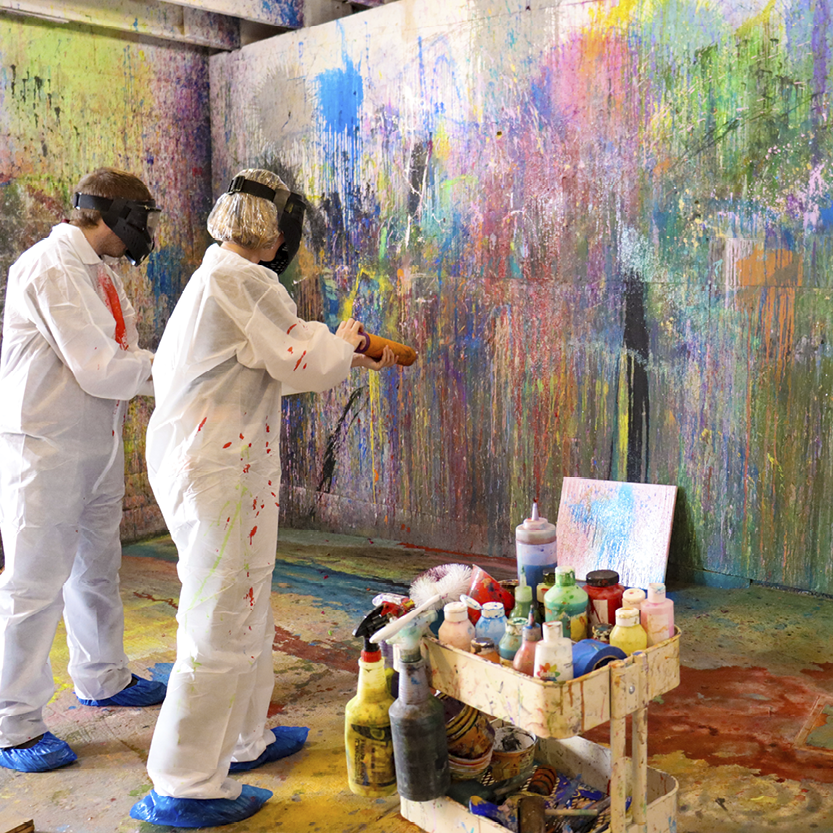 Two people spraying paint in For Arts Sake Rage Room.
