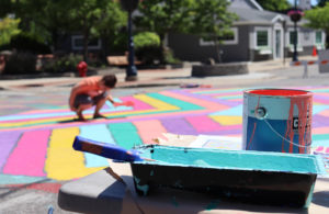 Paint cans and child painting the streets at Paint the Pavement event.