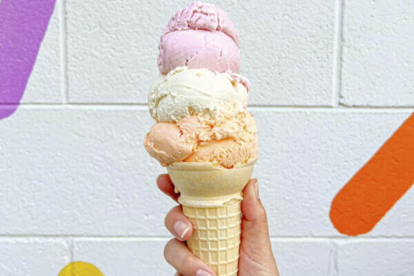 Bright Orange Sherbert, white, and strawberry ice cream scoops in a waffle cone.